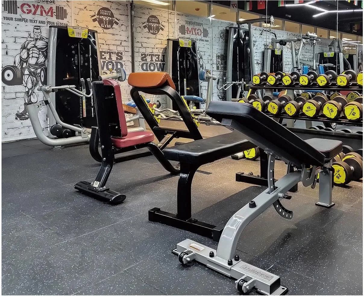Gimnasio con piso de losetas de goma negras con chispas, bancos y mancuernas